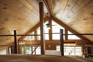 Una habitació de fusta amb sostre alt i inclinat, grans finestres i un llit.