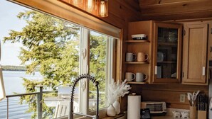A kitchen with a large window, wooden cabinets, and a stainless steel sink. - Red Cedar Haven Lakefront Dock  Kayaks (Sidney)