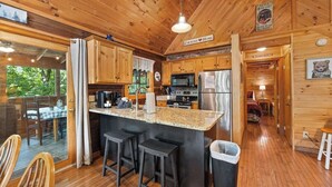 A wooden cabin with a kitchen featuring granite countertops, stainless steel appliances, and a bar area with stools.
