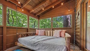 A wooden cabin bedroom with a bed, large windows, and a hanging light fixture.