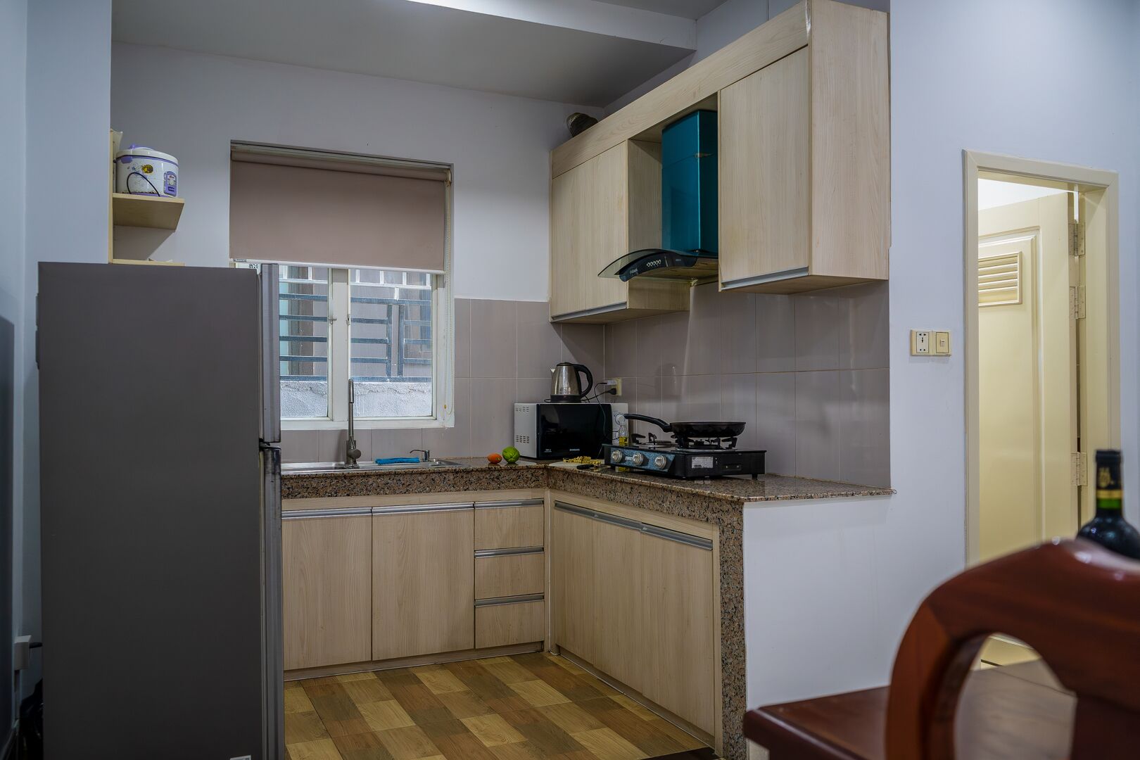 Eine kompakte Küche mit Kühlschrank, Mikrowelle, Herd und einem Fenster mit Jalousien.