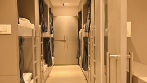 A hotel corridor with bunk beds on either side, a central door, and a ceiling-mounted air conditioning unit. - Bed & Bread Dormitory (Bharuch)