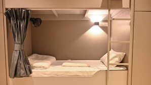 A bunk bed with a curtain, a bedside lamp, and a shelf. - Bed & Bread Dormitory (Bharuch)