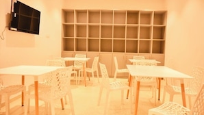 A room with white furniture, including tables and chairs, arranged in a U-shape. - Bed & Bread Dormitory (Bharuch)