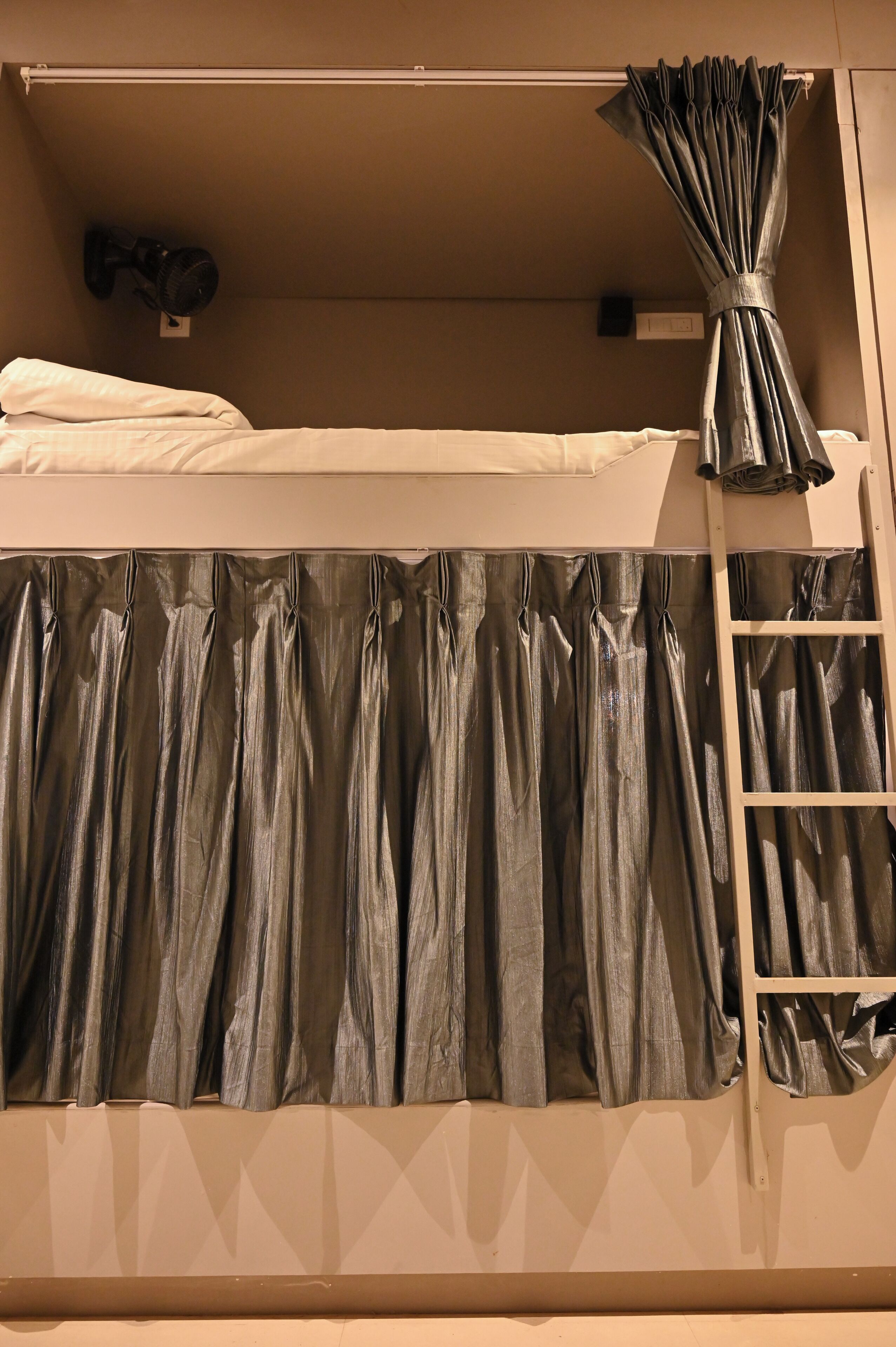 A bunk bed with a ladder on the right, a headboard curtain, and a headboard curtain tied back.