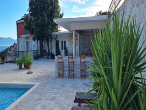 A poolside area with stone flooring, a pool, and outdoor seating. - Holiday Home Mico (Gradac)