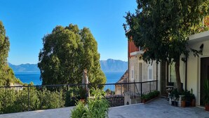 A stone-paved patio with potted plants, a view of the sea, and a building with a balcony. - Holiday Home Mico (Gradac)
