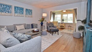 Ein Wohnzimmer mit grauem Sofa, einem Couchtisch, einem gemusterten Teppich und einem blauen Schrank.