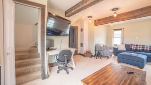 Amplia sala de estar con una mesa de centro de madera, un sofá azul, una silla de oficina gris y una escalera que conduce a otra habitación.