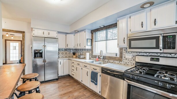 Una cocina moderna con electrodomésticos de acero inoxidable, armarios blancos y una barra de madera.
