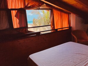 Une chambre avec un lit, une fenêtre avec des rideaux, une chaise et une vue sur la plage.
