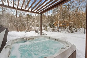 A hot tub in a covered outdoor area with snow-covered trees and a house in the background.