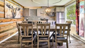 A dining area with a wooden table and chairs, a chandelier, and a kitchen in the background. - Spa - Waterfront - Babyfoot | La Source (Saint-Côme)