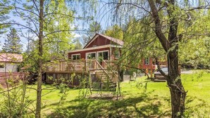 A red cabin with a wooden deck and a swing, surrounded by trees and grass. - Spa - Waterfront - Babyfoot | La Source (Saint-Côme)