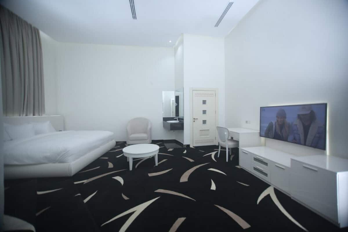 A modern hotel room with a bed, a small round table, a chair, a TV, and a desk.