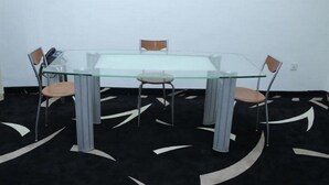 Una mesa con cubierta de vidrio, cuatro sillas, un teléfono y una lámpara de mesa pequeña.