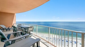 A balcony with a table and chairs, overlooking a beach with people and umbrellas. - New Complex!  BeachFront!  Lazy River/Slide!! (Orange Beach)