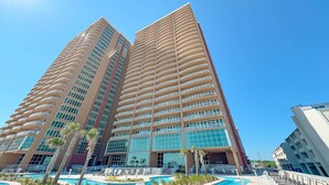 A high-rise hotel with multiple balconies, a swimming pool, and a clear blue sky. - New Complex!  BeachFront!  Lazy River/Slide!! (Orange Beach)
