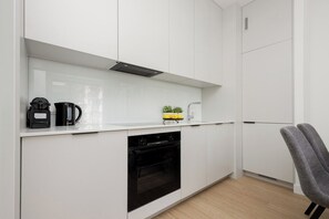 Eine moderne Küche mit weißen Schränken, einem Backofen, einer Kaffeemaschine und einem kleinen Topf mit Pflanze auf der Arbeitsfläche.