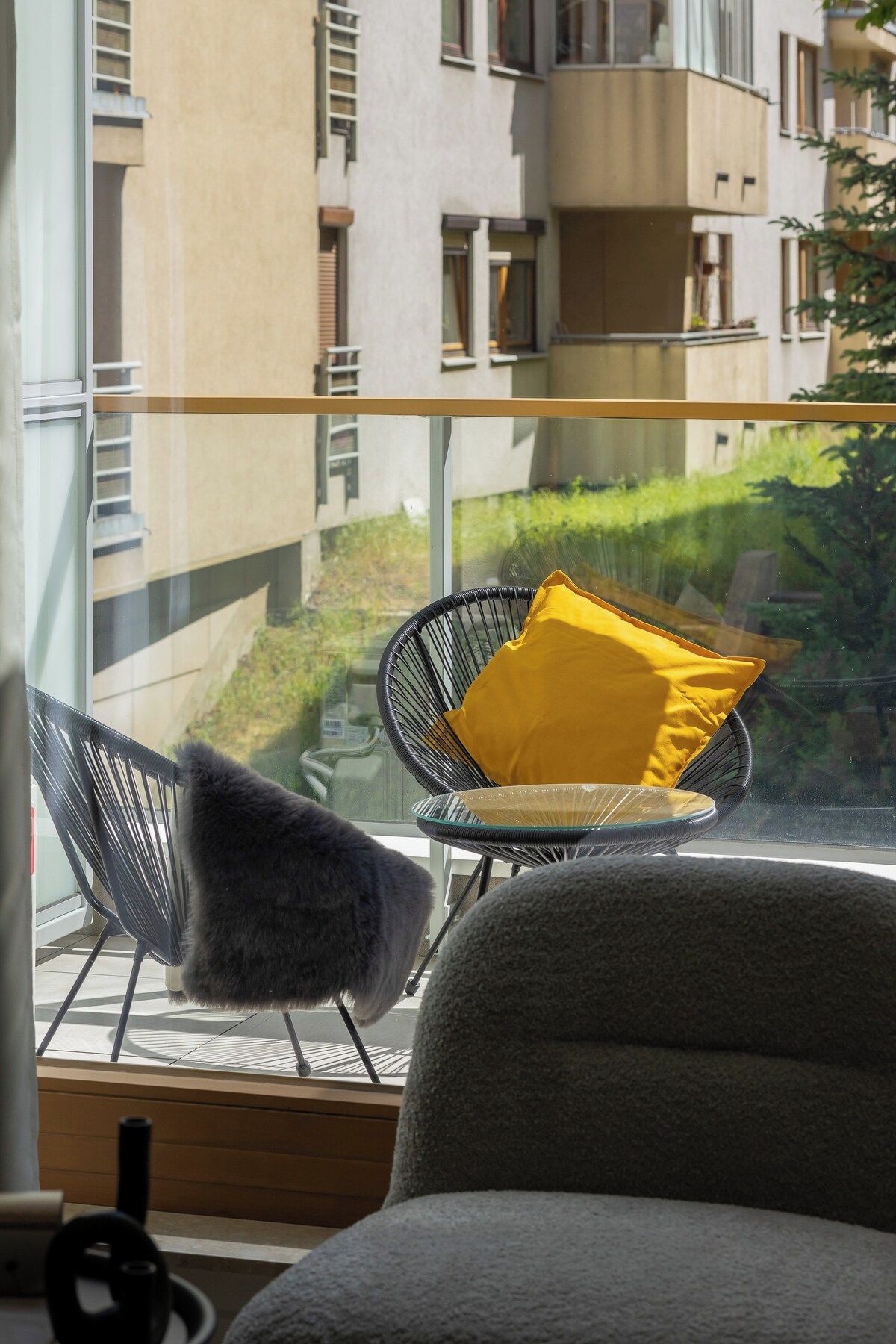 Een balkon met uitzicht op een gebouw en groen. Er staan twee stoelen met kussens.