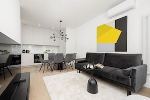 A modern living space with a sofa, dining table, chairs, and a kitchen area. - Warsaw | Domaniewska 24 | Stylish Apartment with Parking | Air Conditioning (Warszawa)