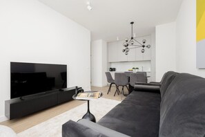 A modern living room with a flat-screen TV, a sofa, and a dining area with chairs and a table.