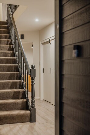 A staircase with carpeted steps and a wooden handrail, leading to a room with a wooden floor and a door.