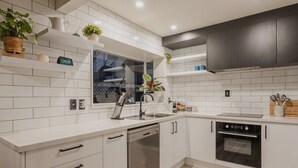 A modern kitchen with white tiles, a dishwasher, an oven, and a window with a view.