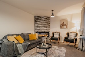 A modern living room with a grey sofa, two armchairs, a coffee table, and a fireplace.