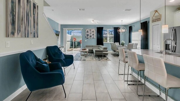 A modern living room with a sofa, blue chairs, a dining area with a table and chairs, and a kitchen with a sink and countertop. - 5BR Home with Private Pool at Storey Lake (Kissimmee)