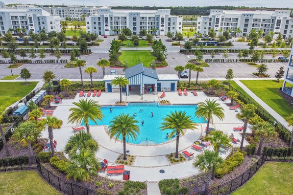 A hotel with a central swimming pool, palm trees, and a parking lot.