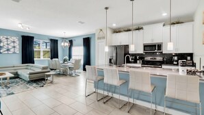 A modern kitchen with white cabinets, stainless steel appliances, and a bar area with white bar stools. - 5BR Home with Private Pool at Storey Lake (Kissimmee)