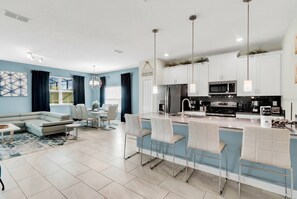 A modern kitchen with white cabinets, stainless steel appliances, and a bar area with white bar stools.