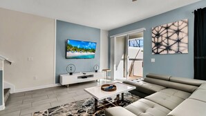 A modern living room with a flat-screen TV, a sofa, a coffee table, and a rug. - 5BR Home with Private Pool at Storey Lake (Kissimmee)