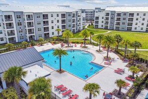 A modern hotel with a central swimming pool surrounded by palm trees and outdoor seating.