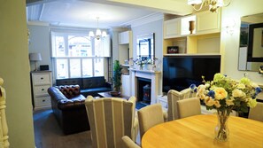 A living room with a fireplace, a sofa, a dining table, and a TV. - 4 Bed House London Hammersmith Fulham Short Let (London)