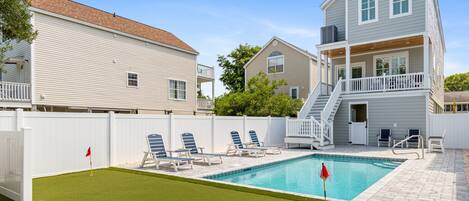 A residential backyard with a swimming pool, a white fence, and a two-story house with a balcony.