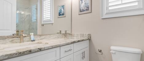 A bathroom with a marble sink, white cabinets, a toilet, and two framed wall art pieces.