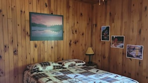A wooden-paneled room with a bed, a ceiling fan, and wall-mounted pictures. - Peaceful sound's of nature!!right outside the east gate of Algonquin park . (Whitney)