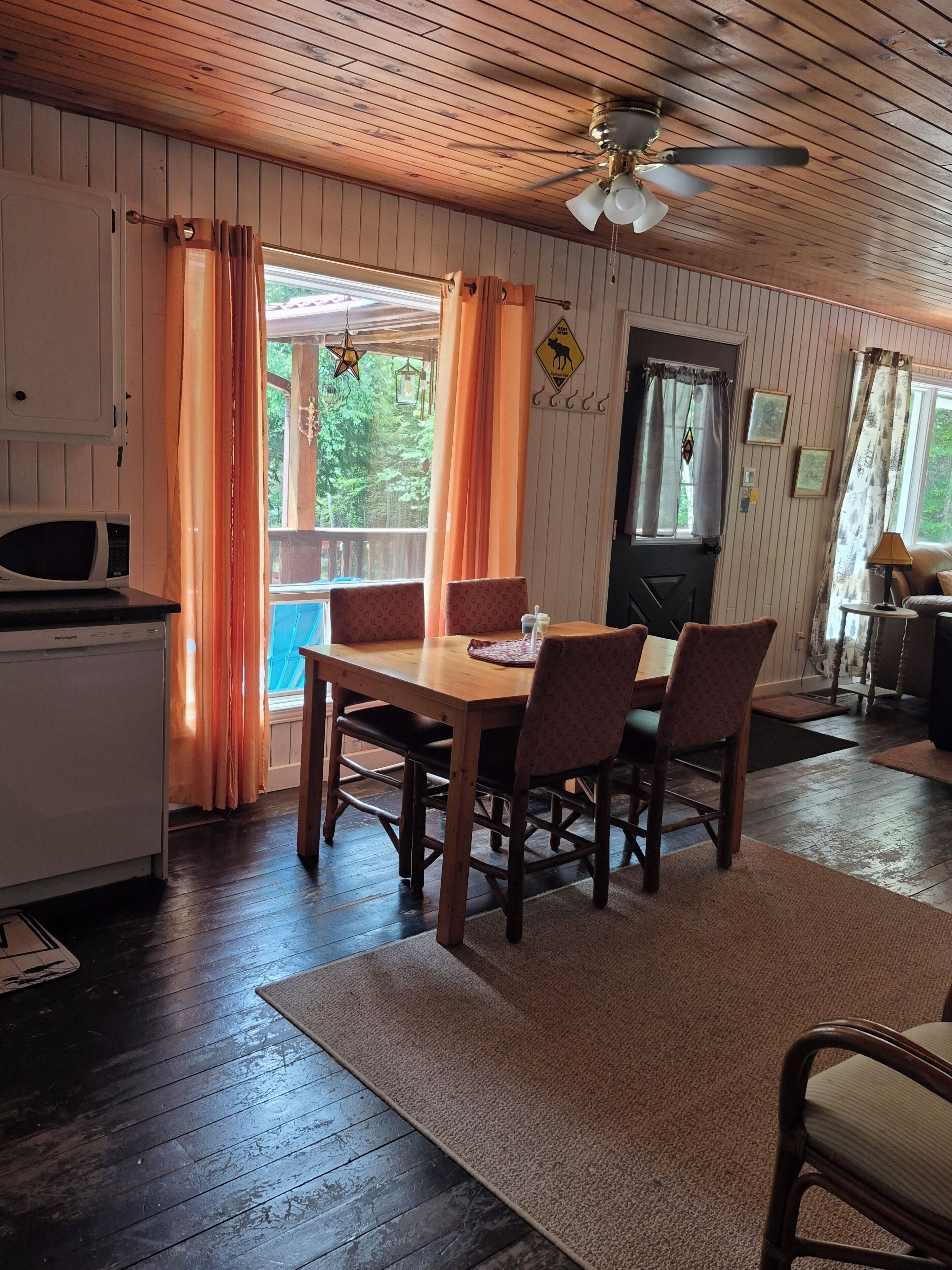 Un espace repas avec une table et des chaises en bois, un ventilateur de plafond et une vue sur l’extérieur.
