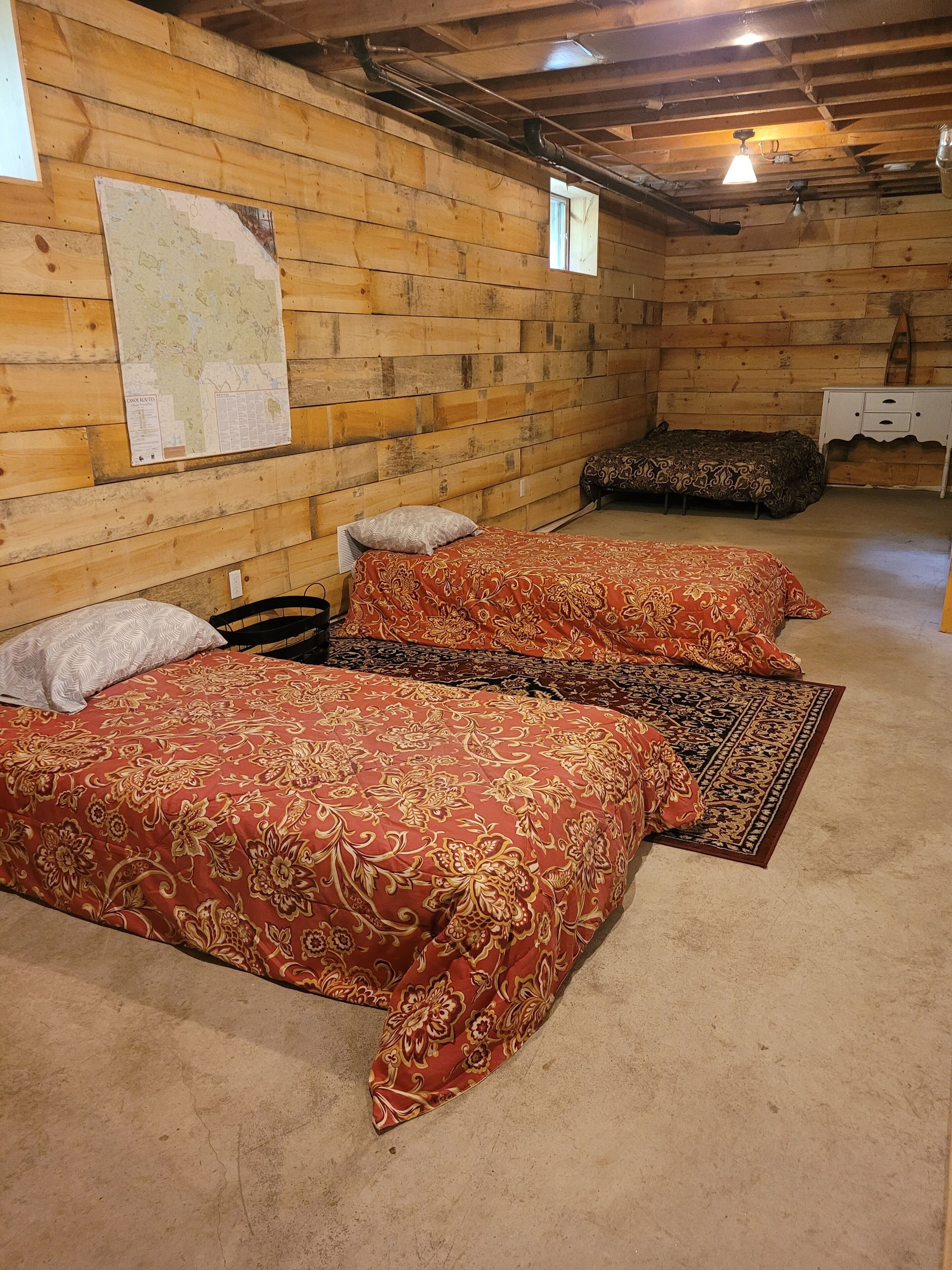 A rustic wooden room with three beds, a map on the wall, and a small white table.