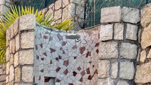 Eine Duschkabine mit Mosaikfliesen, einer Steinwand und einem runden Ablauf.