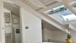 Ein Schlafzimmer mit Dachfenster, einem Bett, einer Topfpflanze, einem gelben Eimer und einem Spiegel.