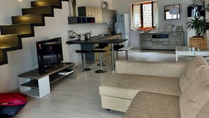 Eine moderne Küche mit einer zentralen Kochinsel, einem Essbereich mit Barhocker, einer Couch und einer Treppe mit freiliegenden Balken.