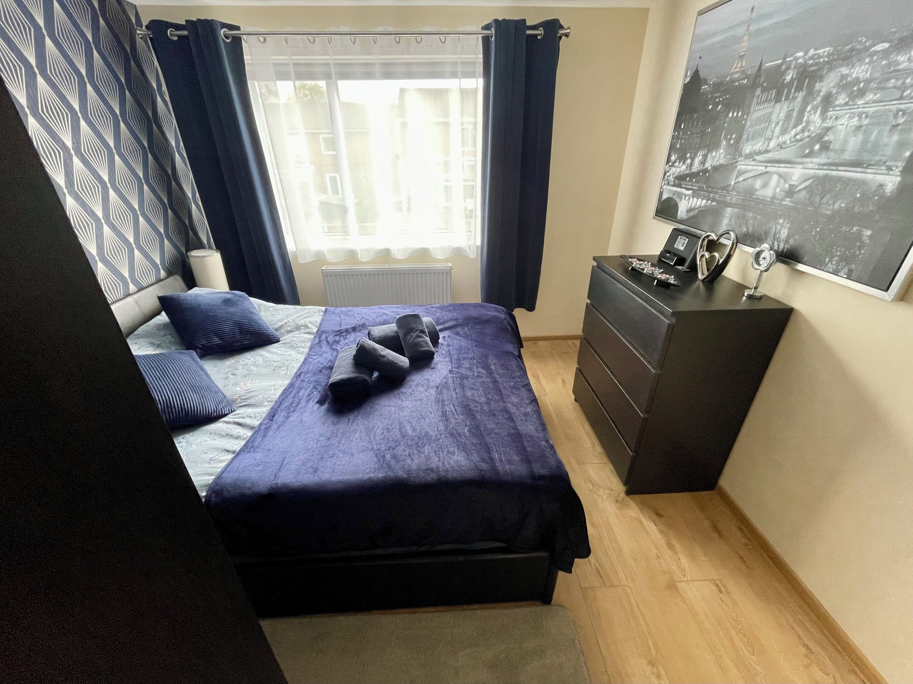 A bedroom with a bed, a dresser, a radiator, and a window with curtains.