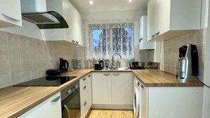 A compact kitchen with white cabinets, a wooden countertop, a built-in oven, a washing machine, and a window with a lace curtain. - Charming 4-Bed Home, Priv Entrance, Garden, Modern Kitchen, Spacious Living Area (Banbury)
