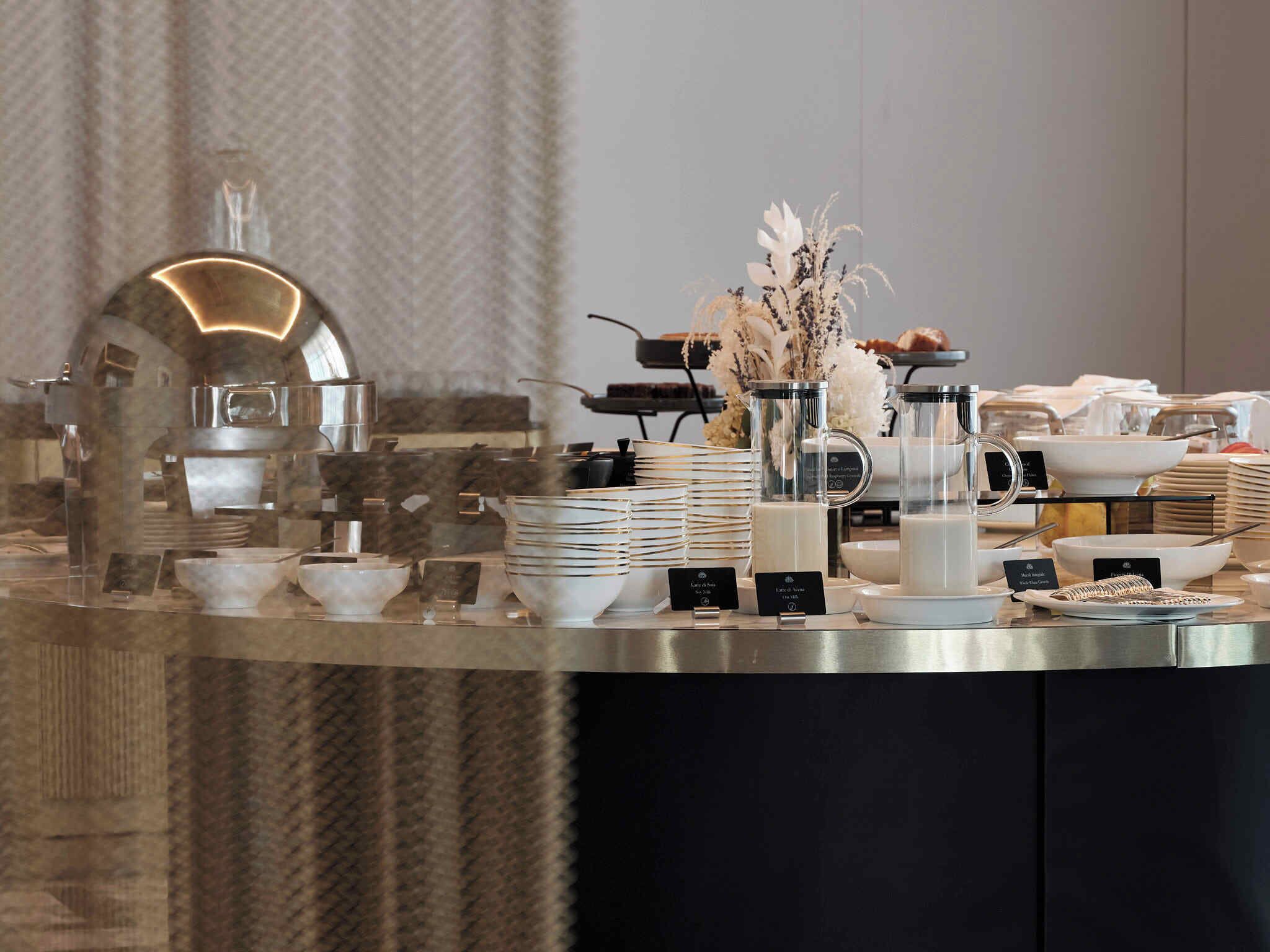 Ein reichhaltiges Buffet mit verschiedenen Speisen und Geschirr, darunter Schüsseln, Teller und eine Kaffeestation.