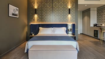 Een moderne hotelkamer met een groot bed, nachtkastje, een bankje, een kitchenette en een decoratief wandpaneel.