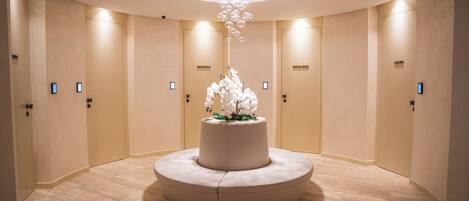 Un hall d’hôtel doté d’un espace salon central circulaire, d’un luminaire décoratif suspendu et de portes portant les inscriptions « AMAZONIE », « MONTE ROSA » et « LAGUNA ».