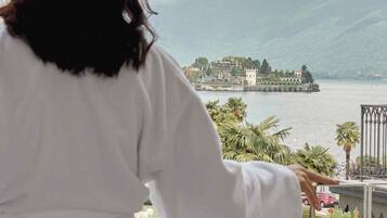 A person in a white robe overlooking a scenic view of a body of water, a distant island, and mountains.
